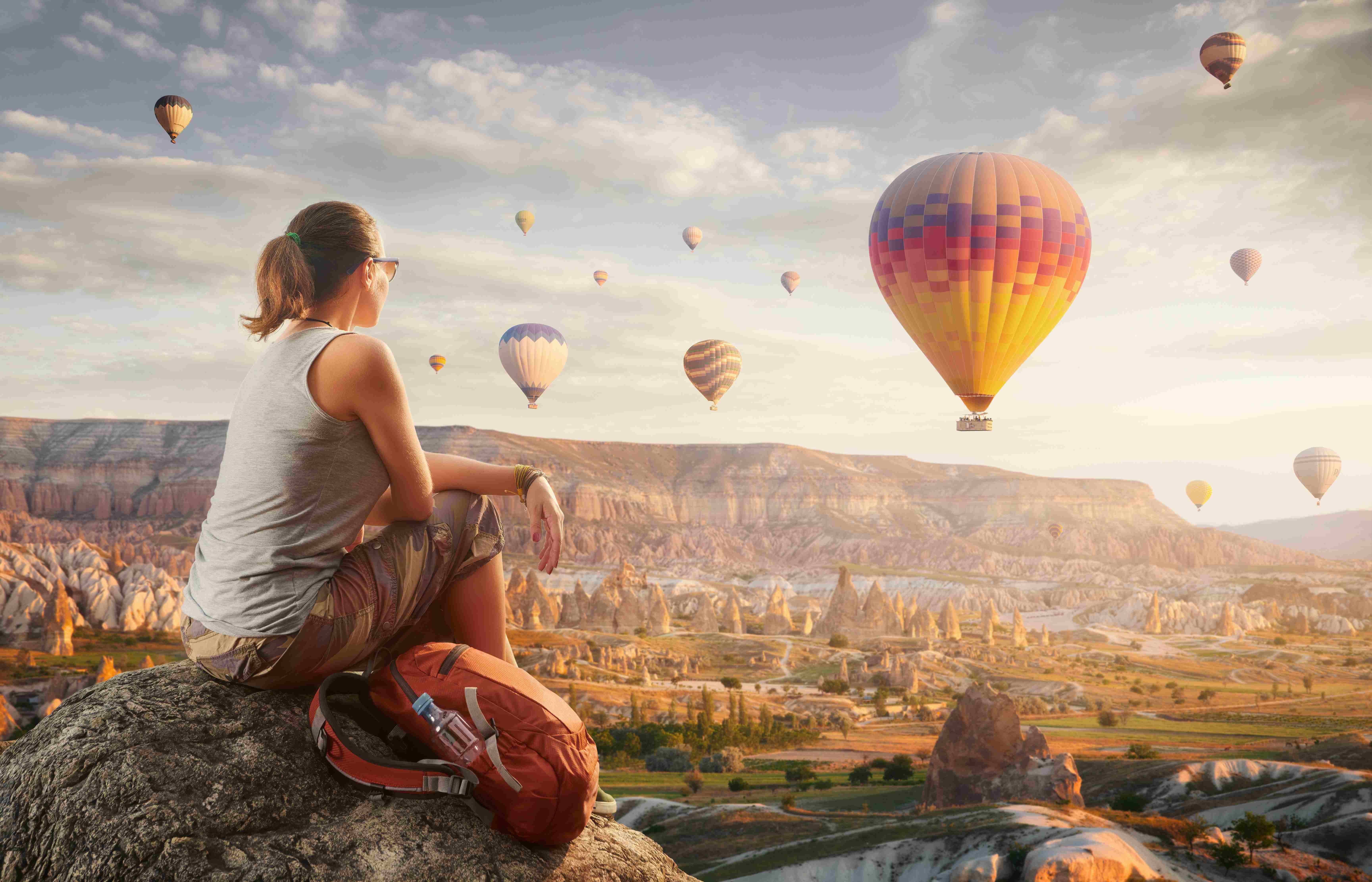 Traveler watching colorful hot air balloons flying over the unique rock formations and valleys of Cappadocia, Turkey at sunrise